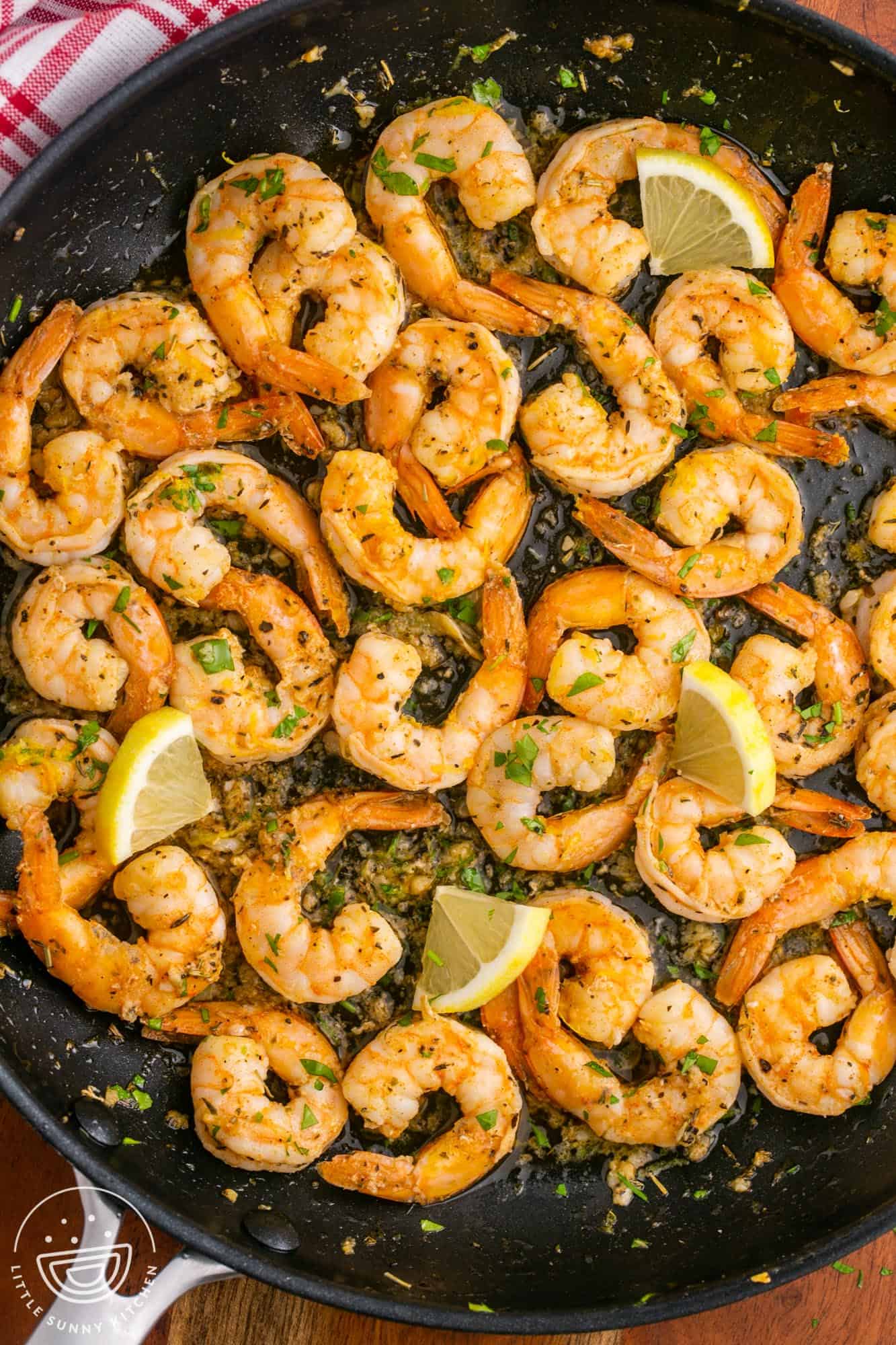 a frying pan of cooked pan seared shrimp with seasonings and thin lemon slices