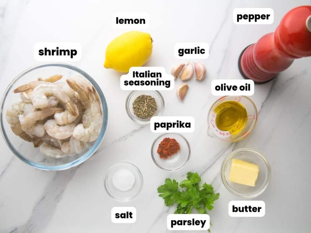 The ingredients needed to make the best pan seared shrimp, in small bowls on a marble counter. Each ingredient is labeled with a white text box.