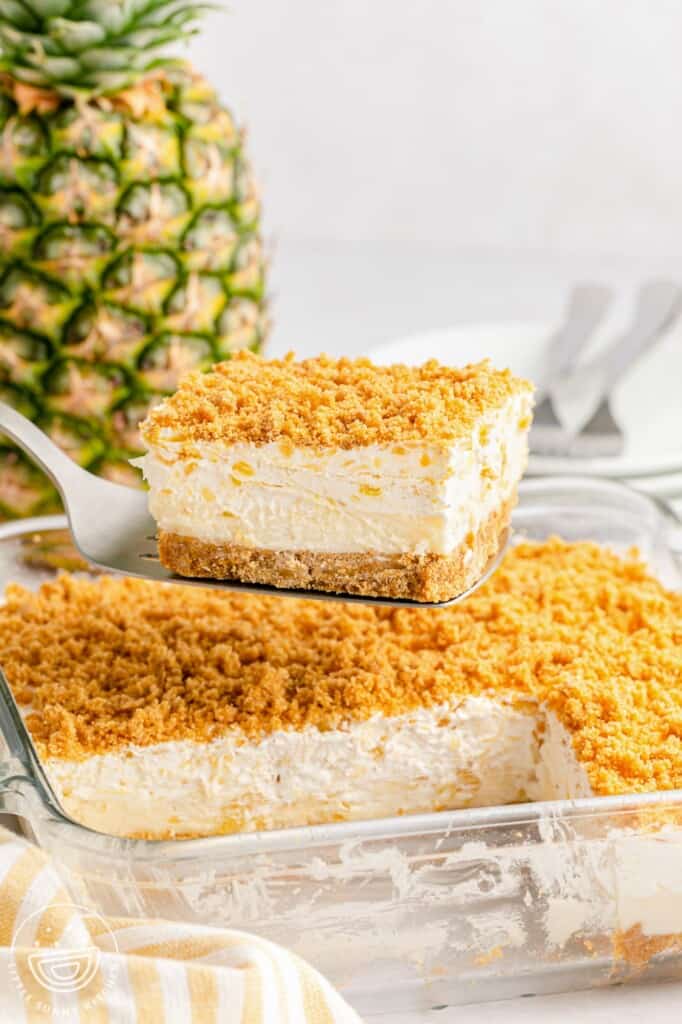 Taking a slight of the pineapple dessert from a glass pan