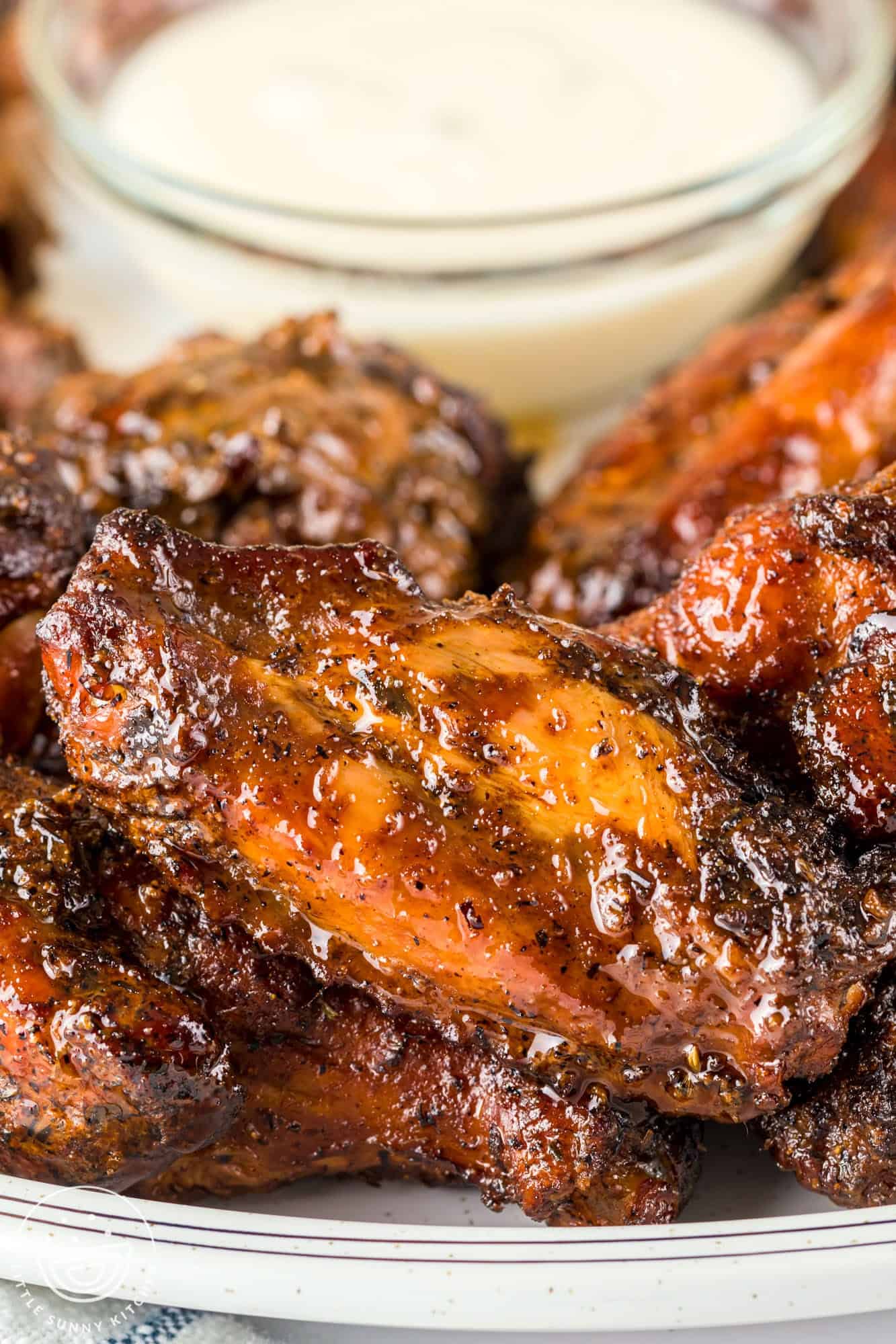 Close up shot of a smoked chicken wing, the flat piece, and ranch dip in the background.