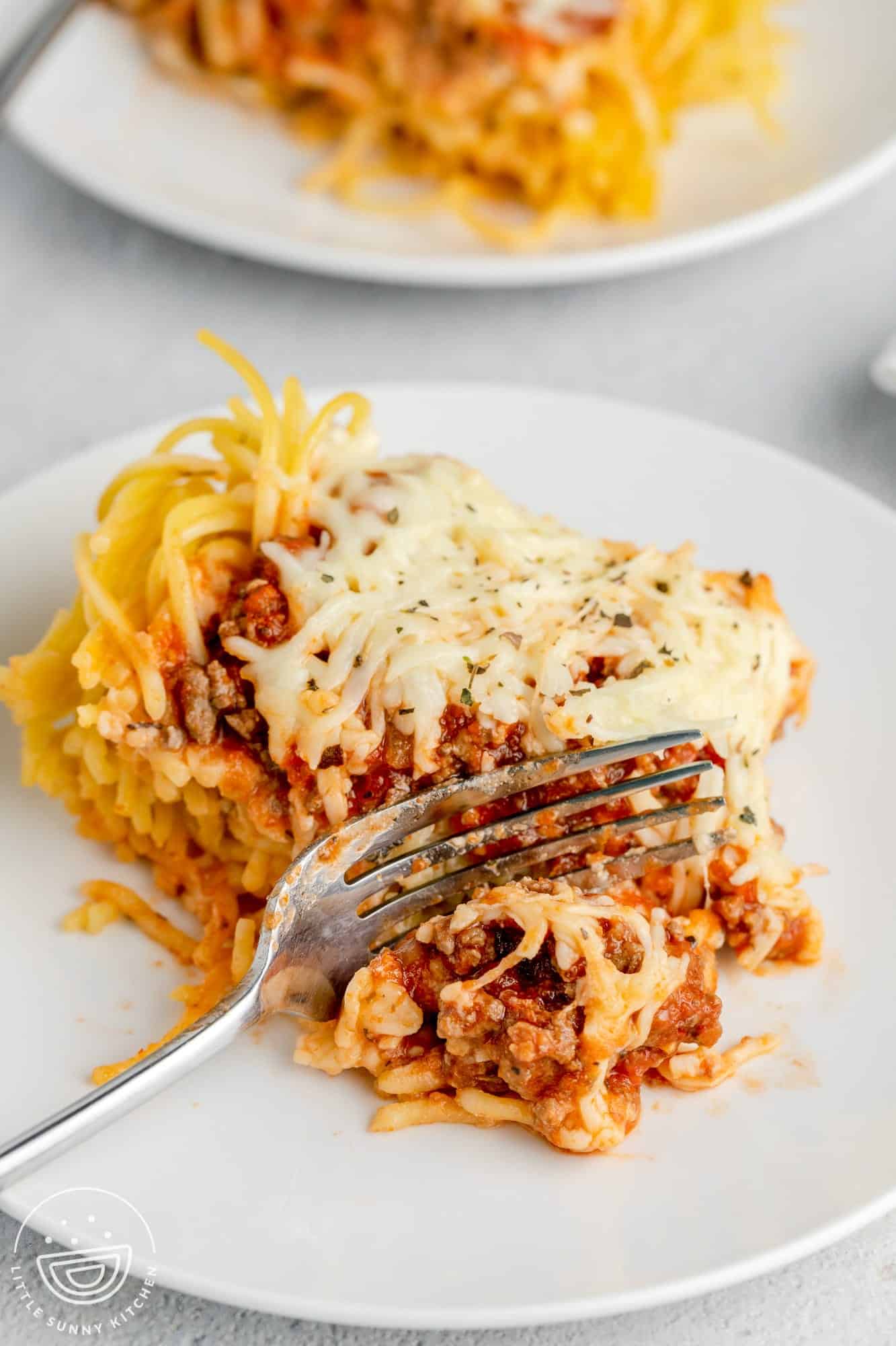 a serving of spaghetti pie on a dinner plate. A fork is picking up a bite.
