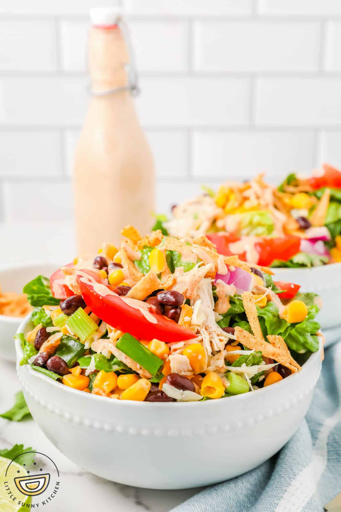 two bowls of tex mex salad with creamy dressing in a bottle in the background