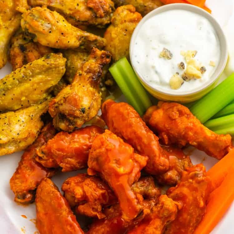 Two flavors of wings on a paper lined platter with a side of blue cheese dressing and carrot and celery sticks