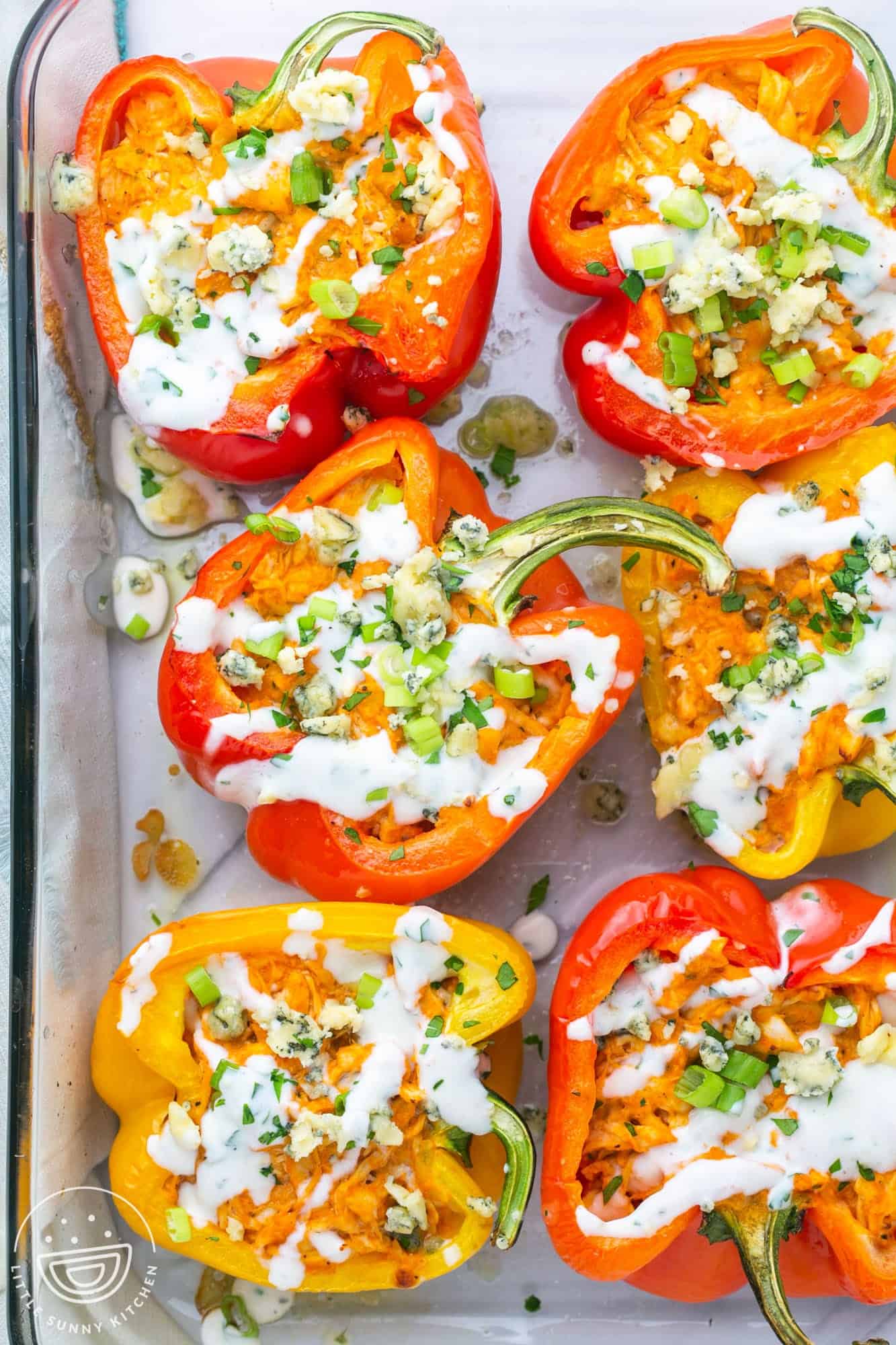 Red and yellow bell peppers, cut in half and baked, stuffed with buffalo chicken and blue cheese. There are six pepper halves in a glass baking dish.