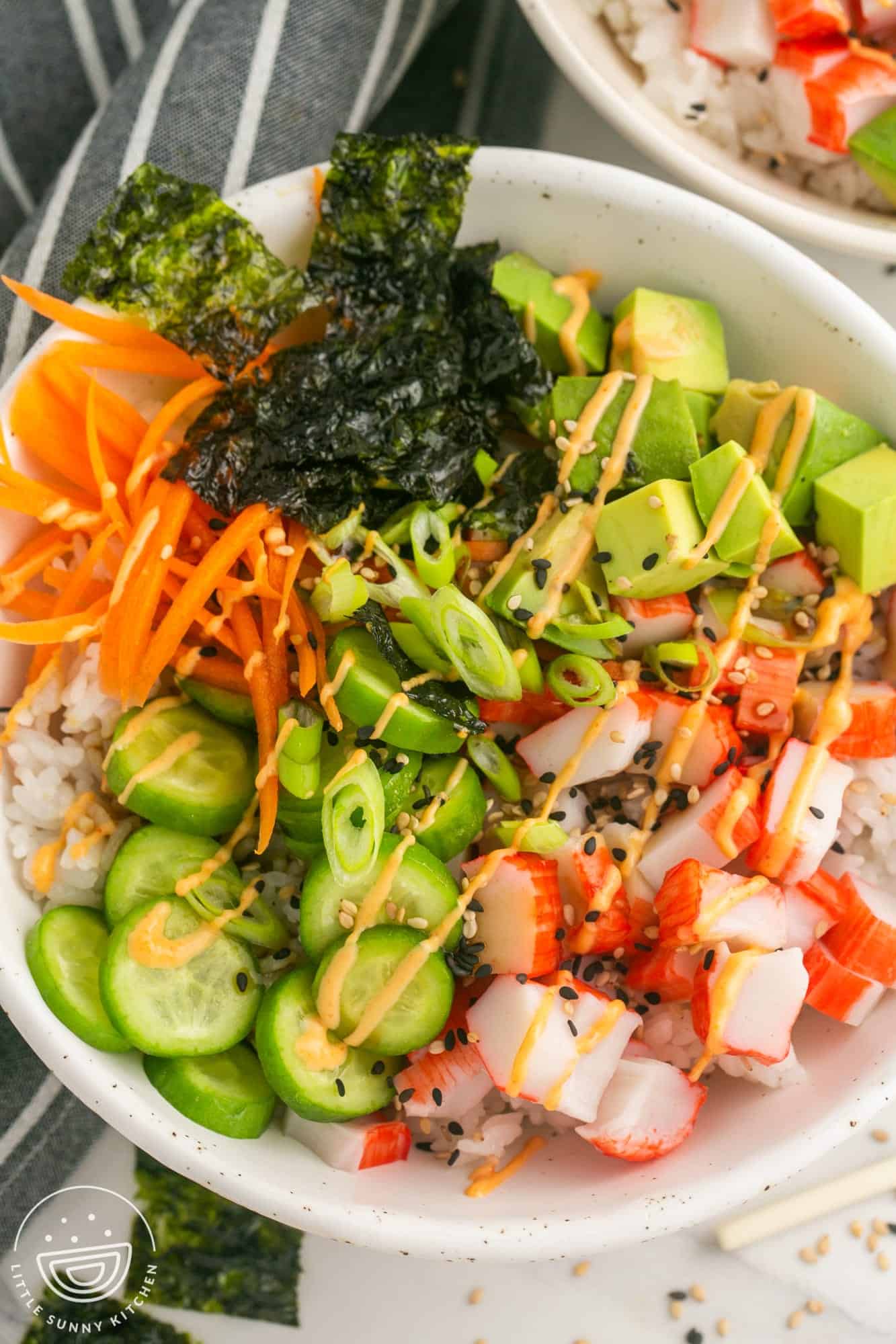 a sushi rice bowl topped with imitation crab, veggies, avocado, and spicy mayo