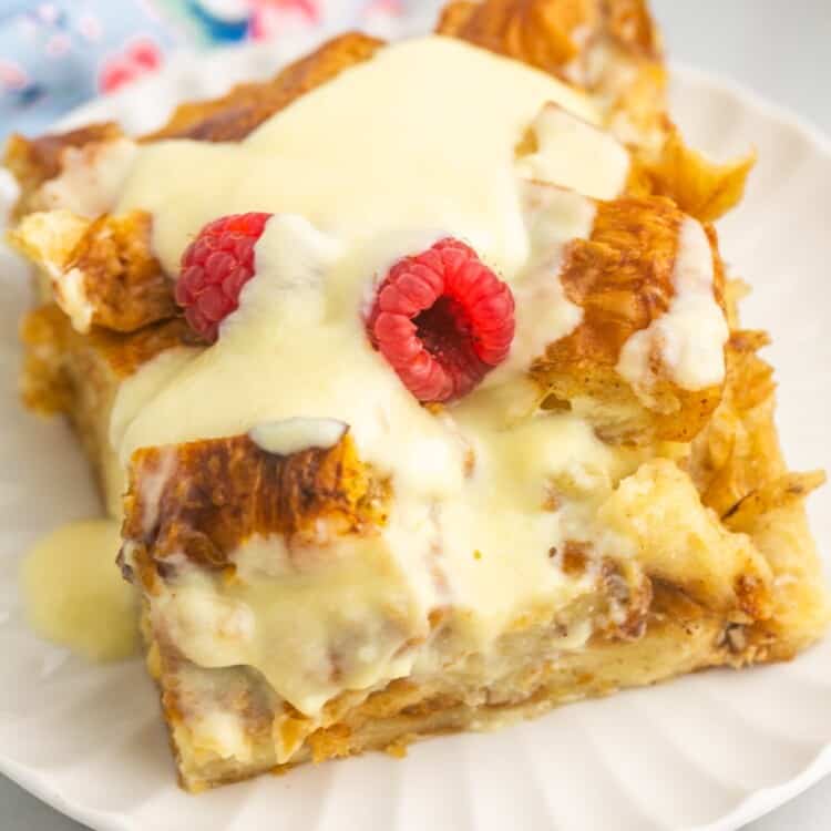 a square piece of croissant bread pudding topped with creme anglaise and raspberries.