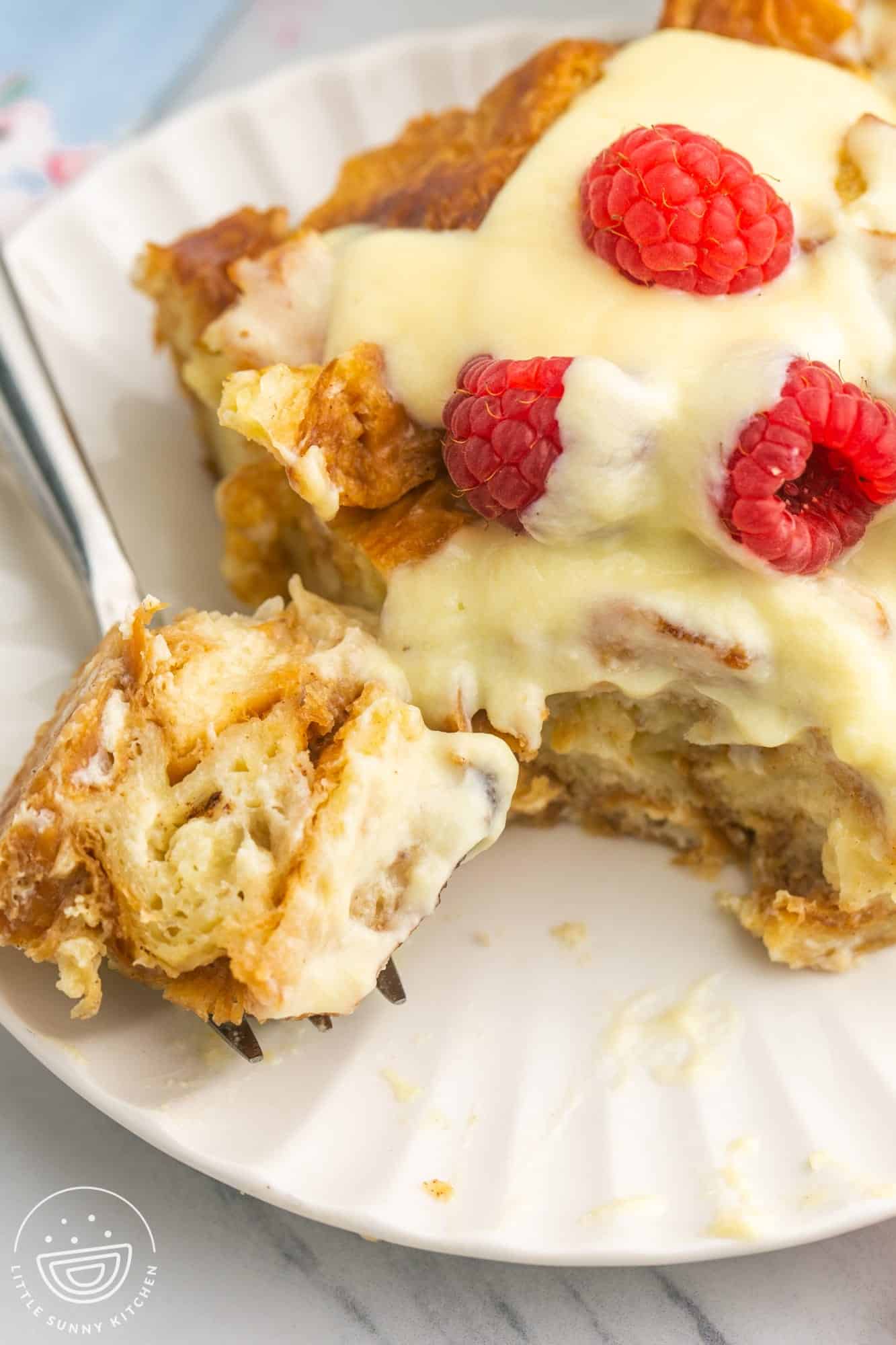 a piece of croissant bread pudding topped with creme anglaise and raspberries.