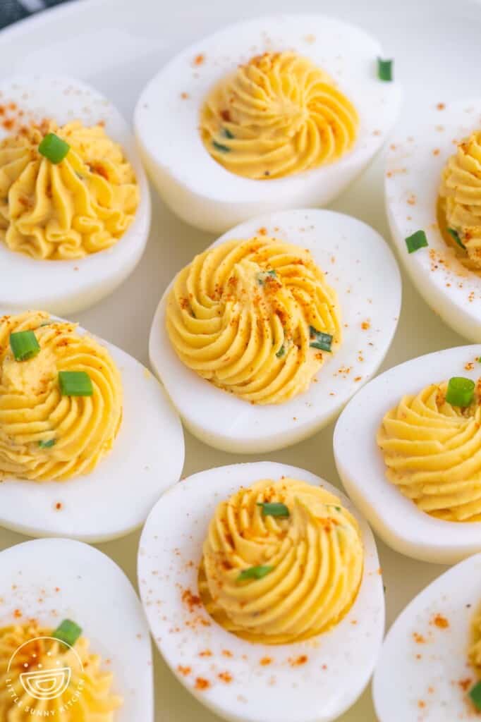a closeup view of a plate of deviled hard boiled eggs with swirled filling, topped with chives and paprika