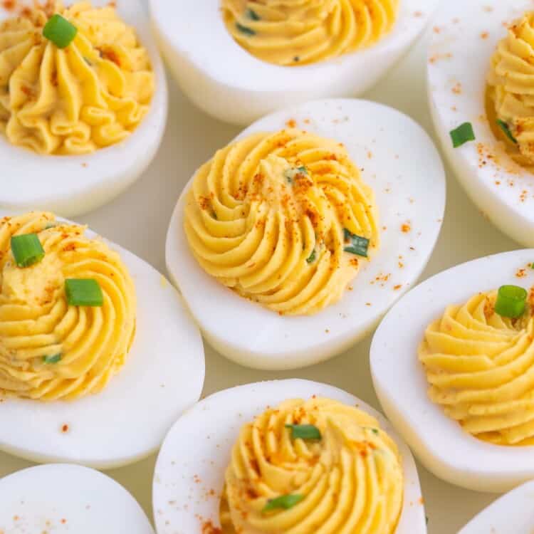 a closeup view of a plate of deviled hard boiled eggs with swirled filling, topped with chives and paprika