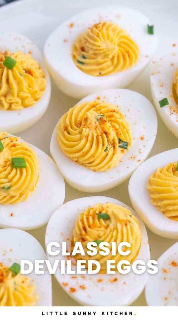 a closeup view of a plate of deviled hard boiled eggs with swirled filling, topped with chives and paprika. Text overlay says "classic deviled eggs"