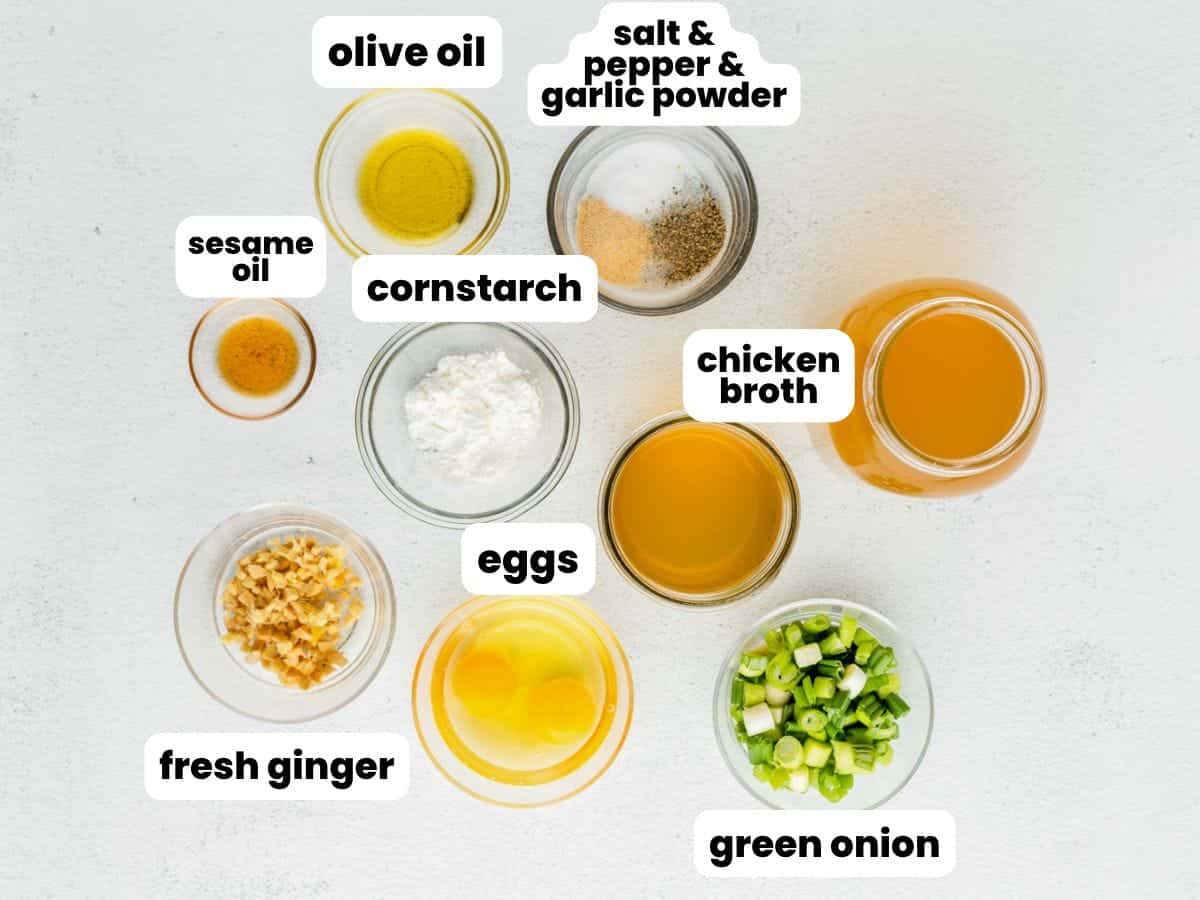 The ingredients needed to make egg drop soup, all in small bowls, viewed from overhead and labeled with white text boxes