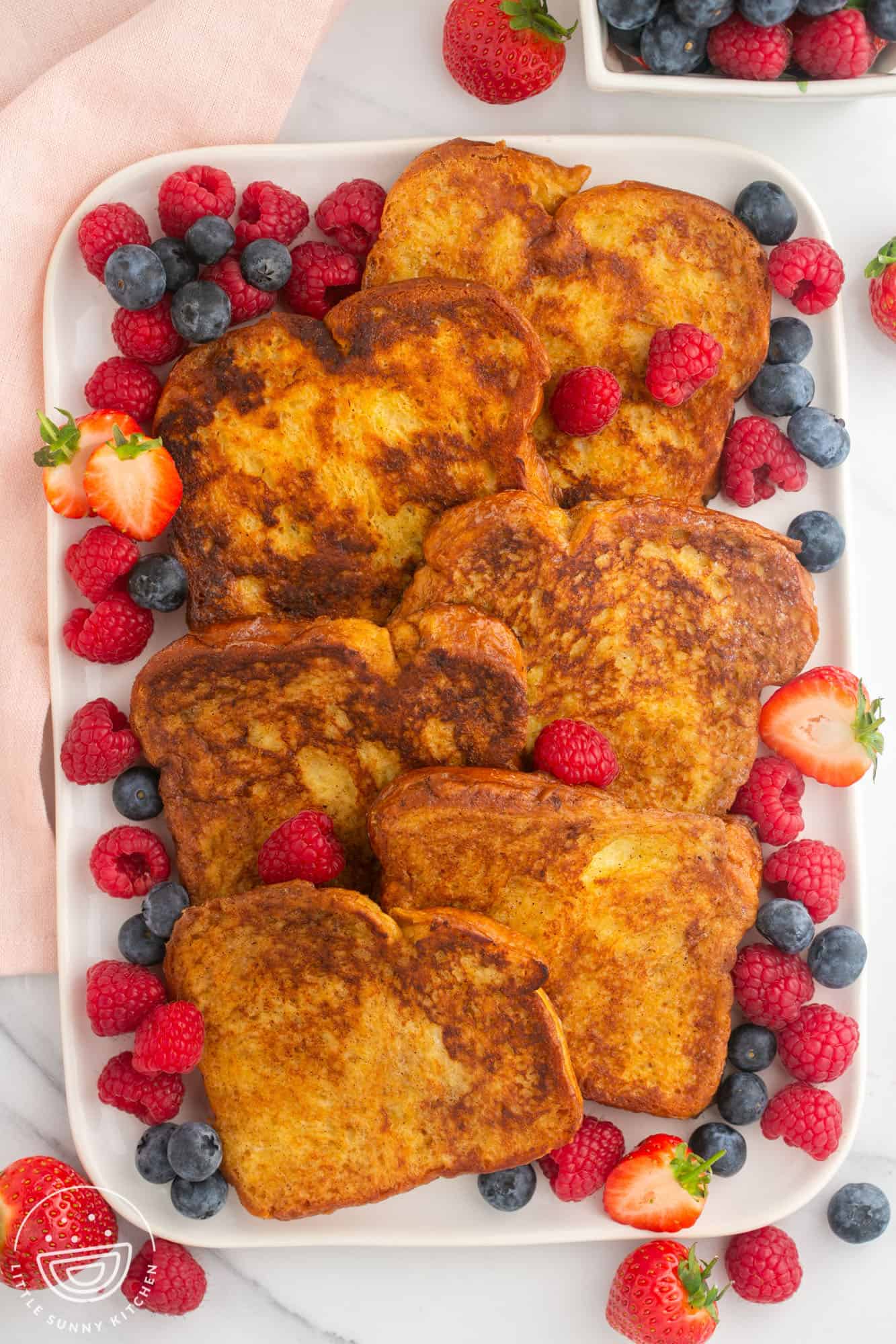 a large white platter filled with french toast slices and fresh mixed berries.