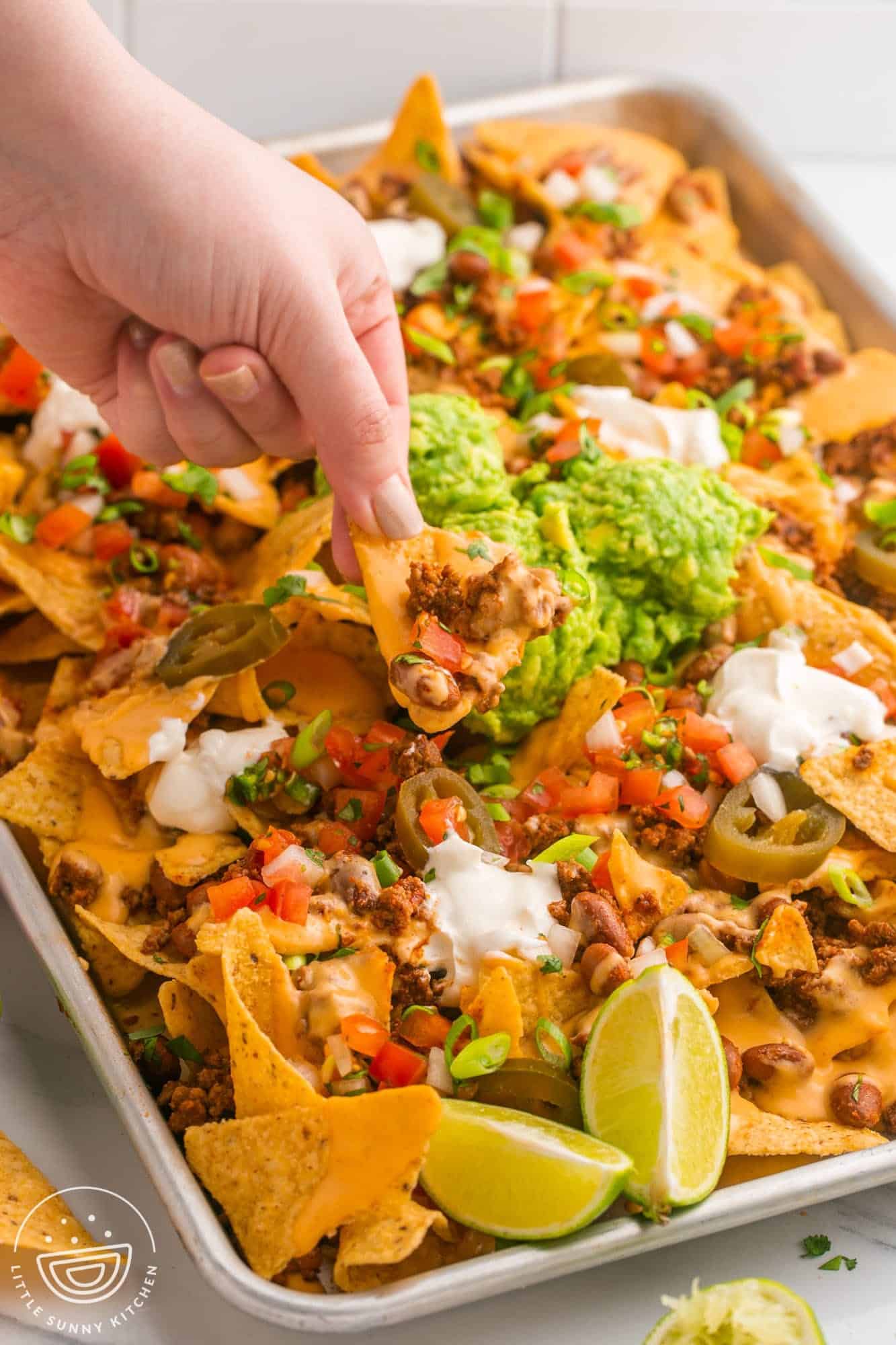 a tray of loaded nachos. A hand is picking up a chip topped with cheese and beef. 
