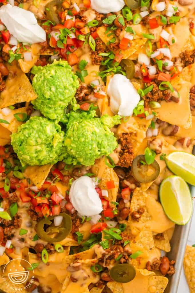 Closeup view of a tray of loaded beef nachos with guacamole, sour cream, and salsa on top.