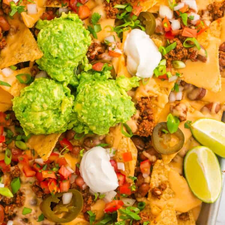 Closeup view of a tray of loaded beef nachos with guacamole, sour cream, and salsa on top.