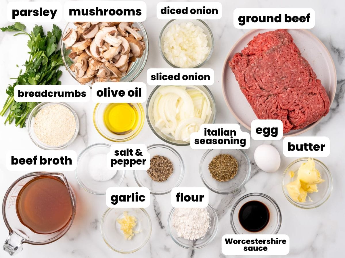 Ingredients needed to make hamburger steaks including ground beef, mushrooms, onion, garlic, butter, beef broth, flour, olive oil, salt and pepper, italian seasoning, breadcrumbs, and parsley.