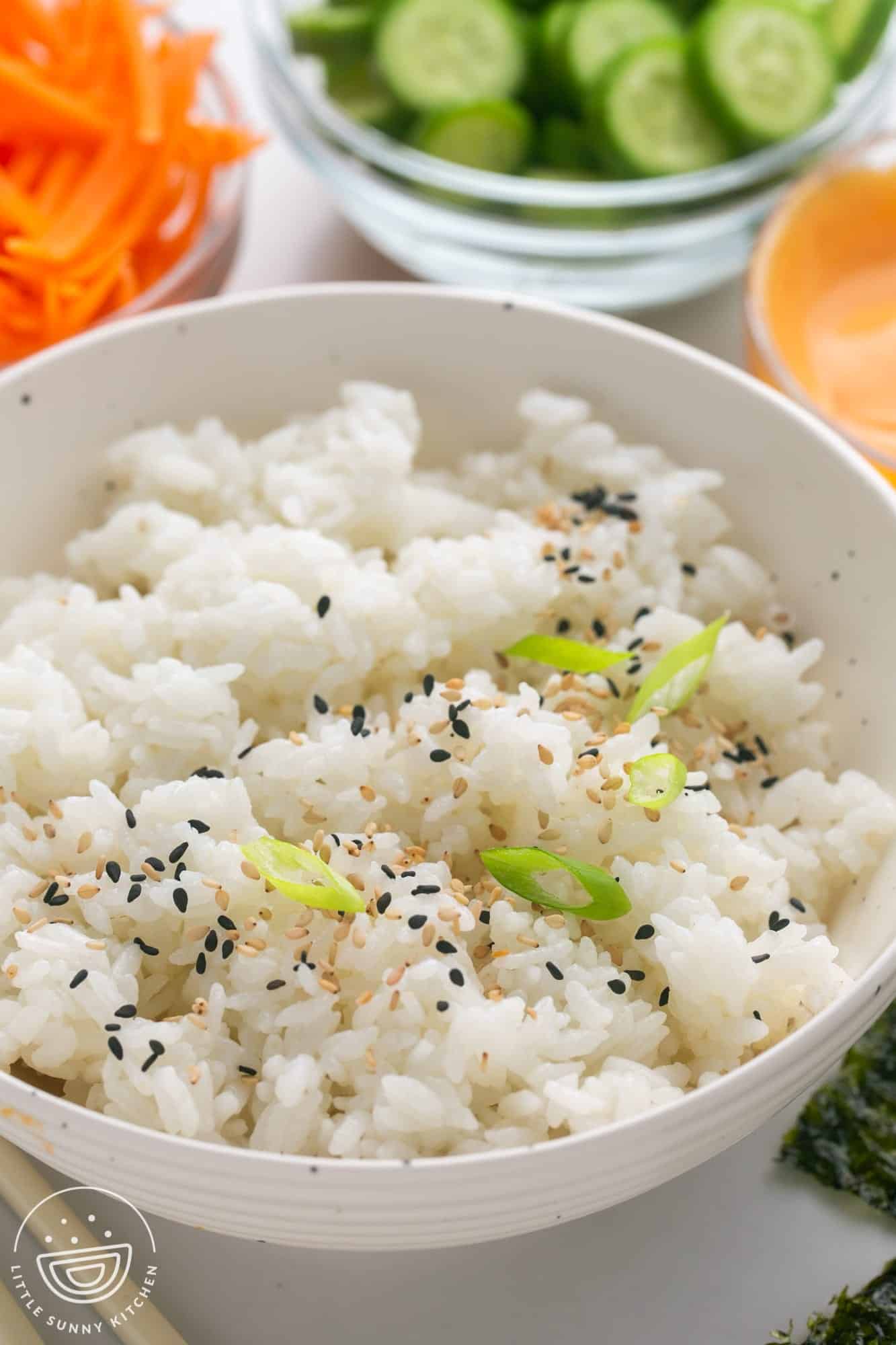 a bowl of cooked sushi rice topped with black and white sesame seeds and sliced green onions
