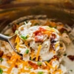 a large spoon holding a scoop of creamy crack chicken with cheese and bacon over an instant pot.