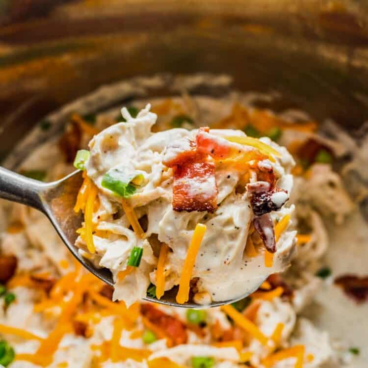 a large spoon holding a scoop of creamy crack chicken with cheese and bacon over an instant pot.