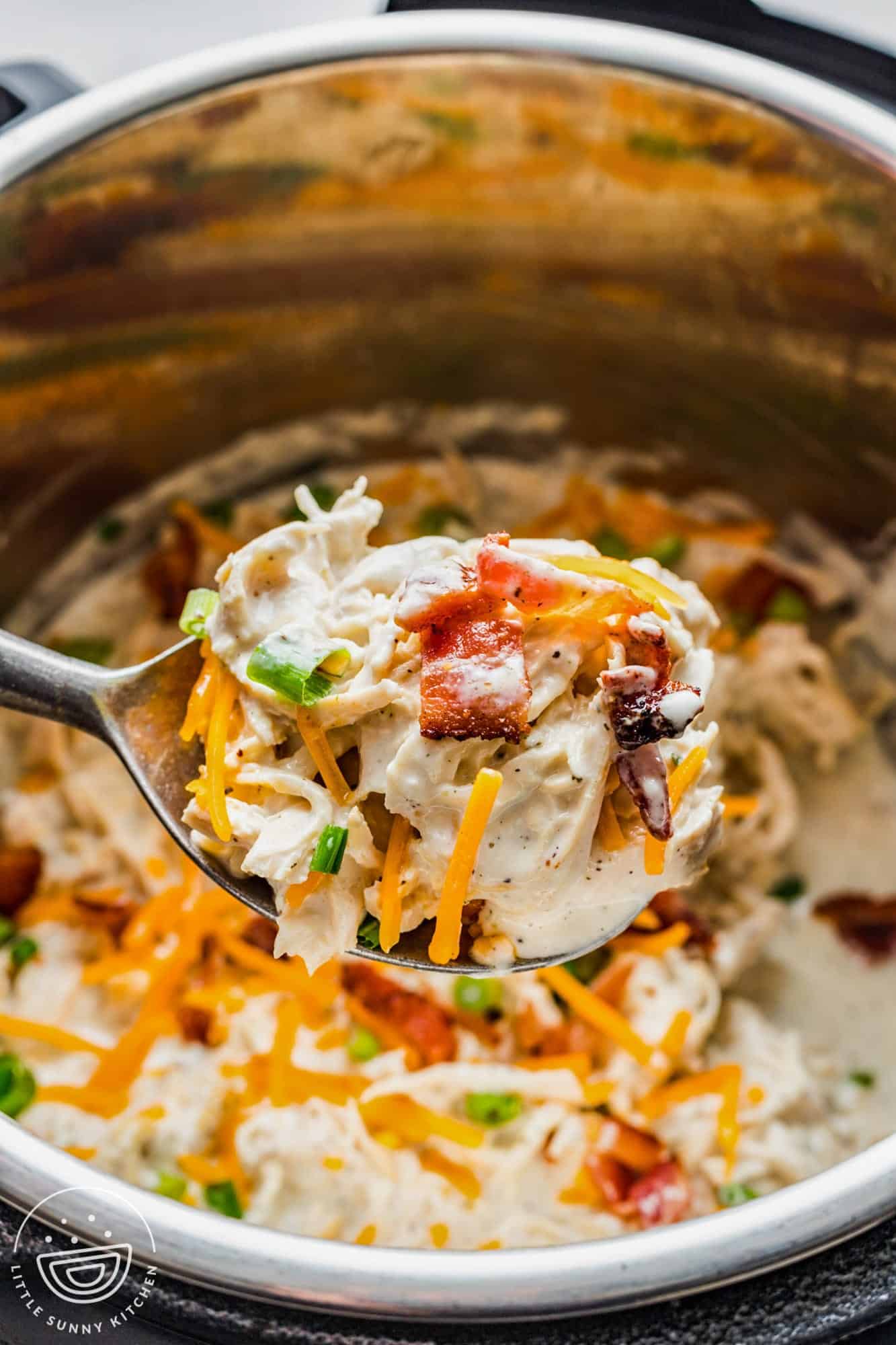 a large spoon holding a scoop of creamy crack chicken with cheese and bacon over an instant pot.