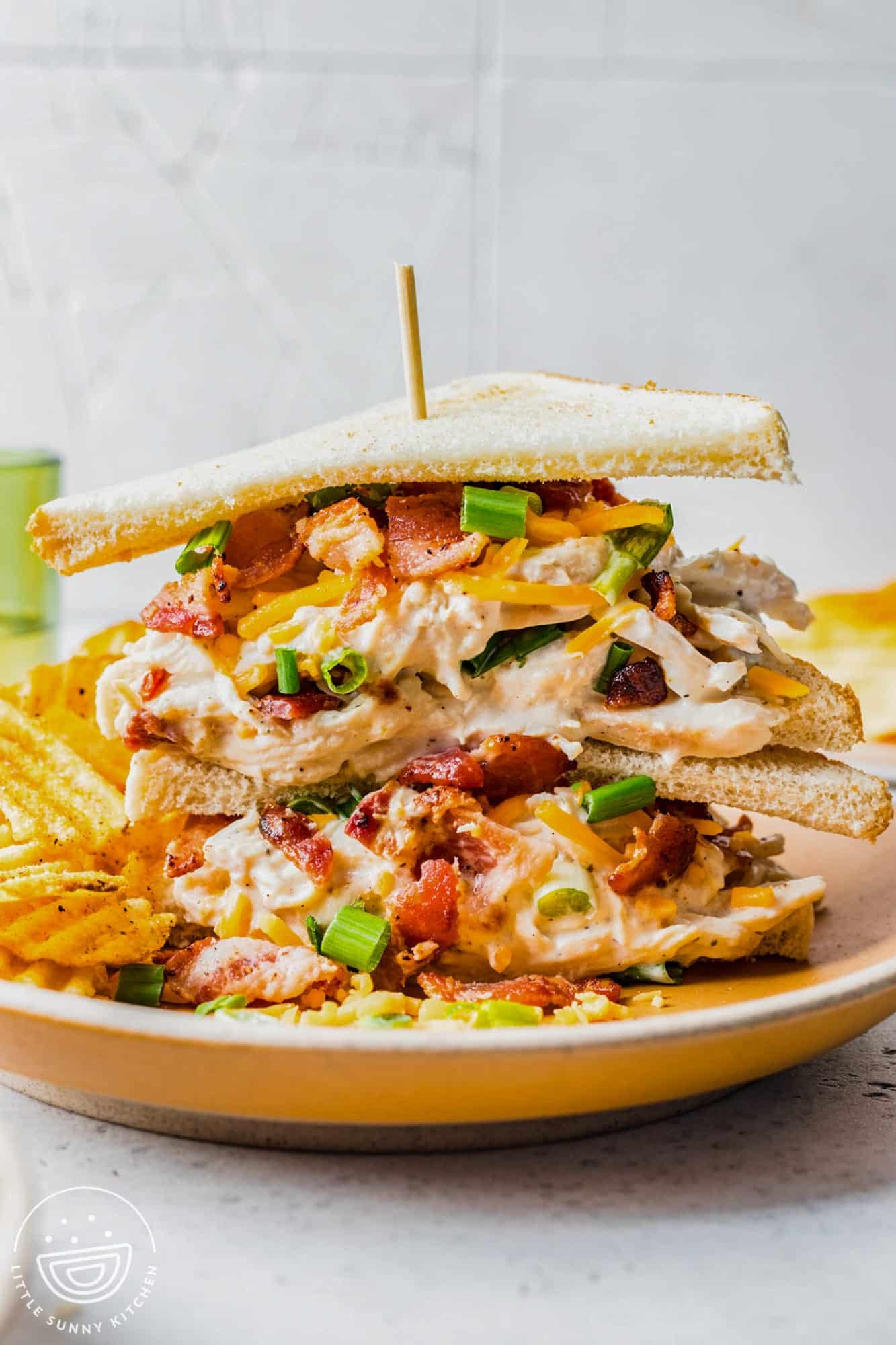 crack chicken sandwiches on thin toasted bread, two sandwiches on top of each other with a skewer holding them together.