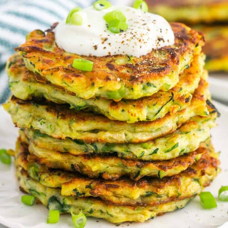 a stack of fried zucchini fritters topped with sour cream and sliced green onion.