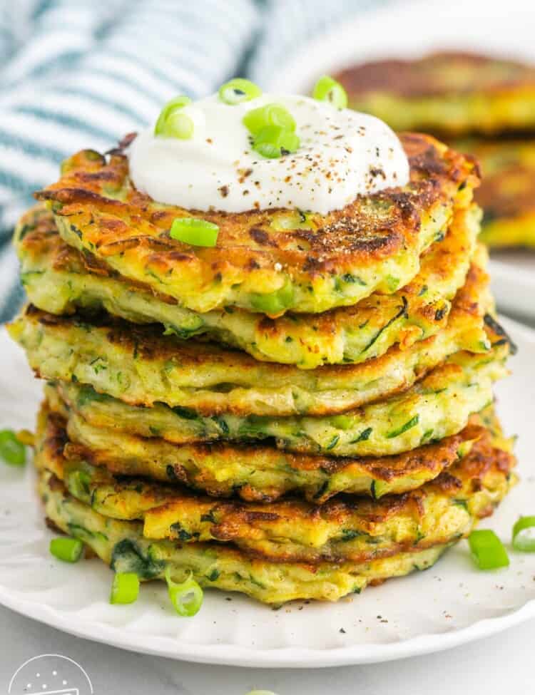 a stack of fried zucchini fritters topped with sour cream and sliced green onion.