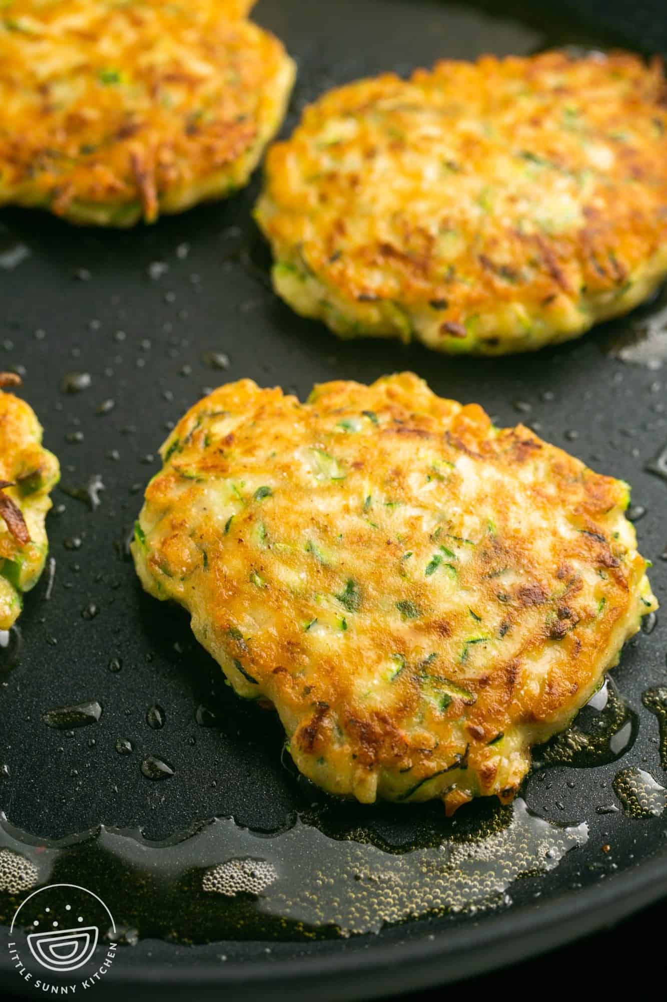 Zucchini fritters frying in a non-stick pan.