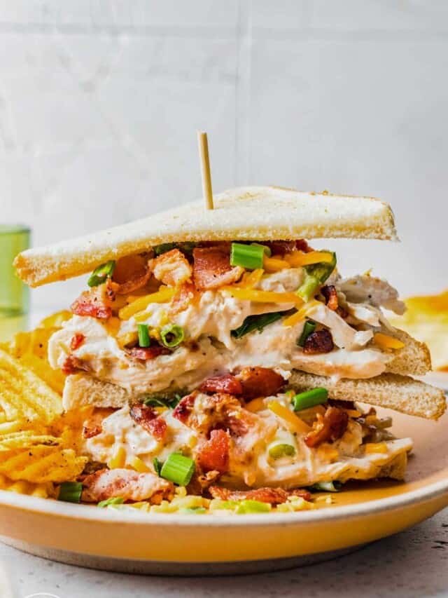 crack chicken sandwiches on thin toasted bread, two sandwiches on top of each other with a skewer holding them together.