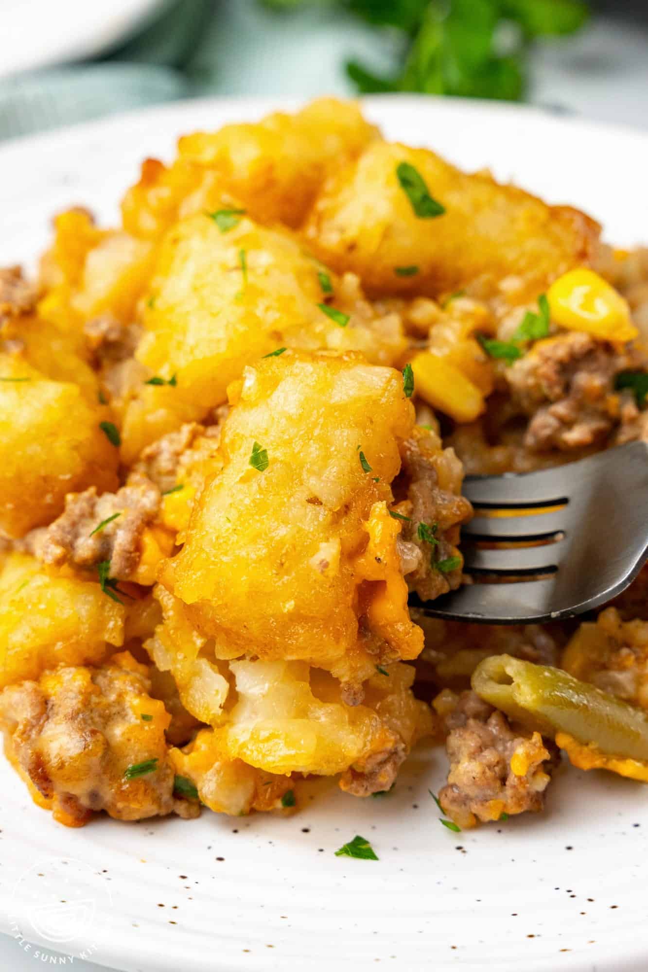 tater tot casserole on a plate, a fork is picking up a bite.