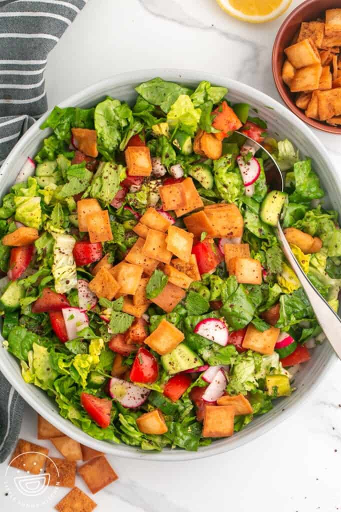 a serving bowl of salad topped with fried pita chips, viewed from overhead.