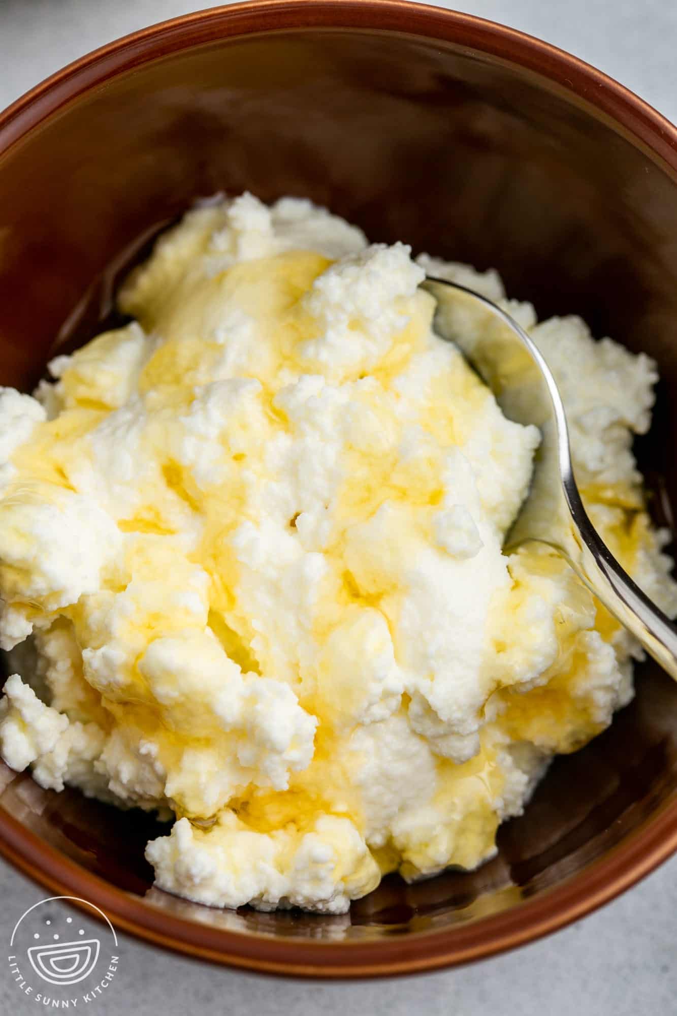 A brown bowl filled with ricotta cheese and drizzled with honey.