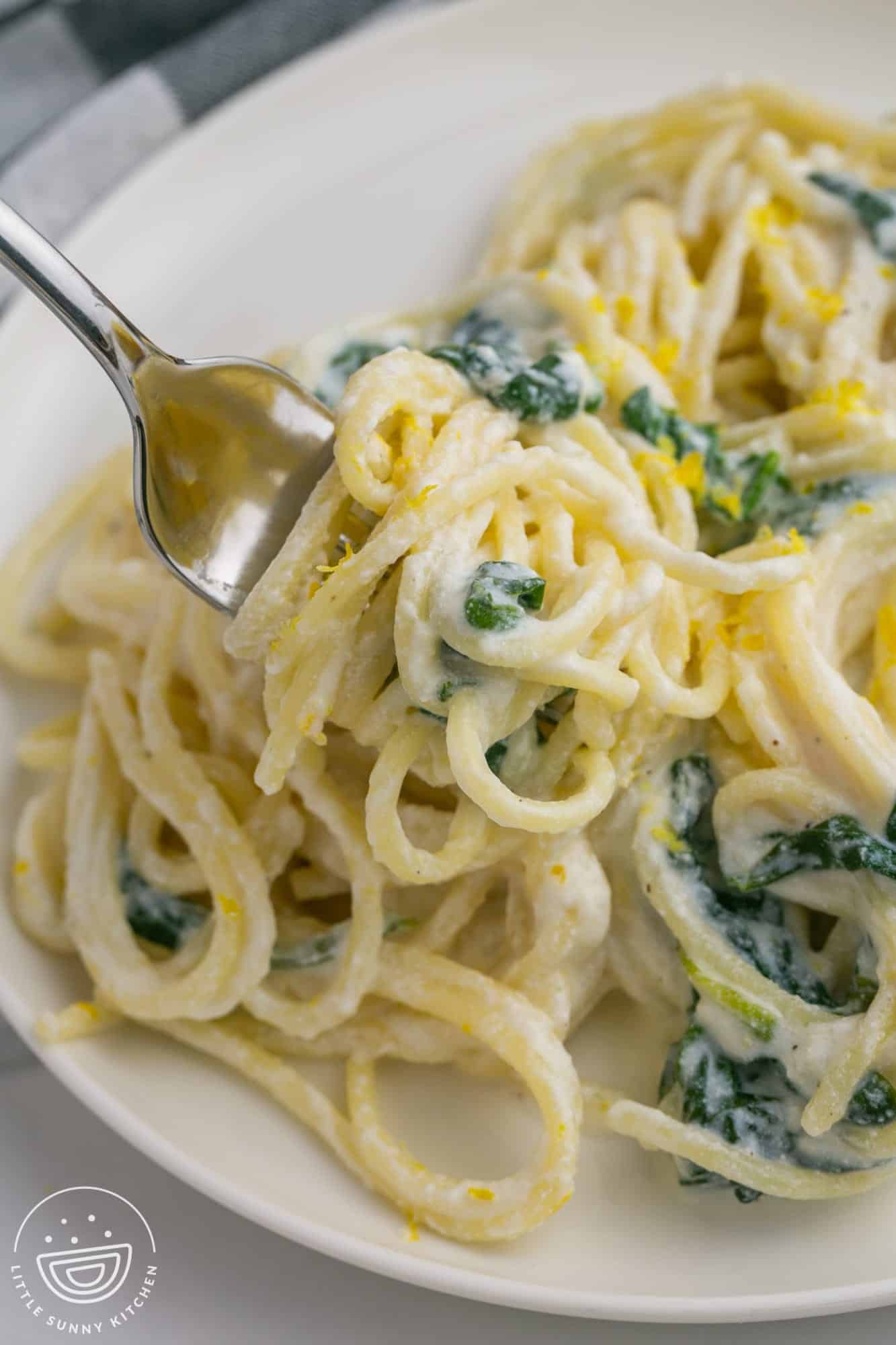 creamy lemon ricotta pasta with spinach on a plate, being picked up with a fork. .