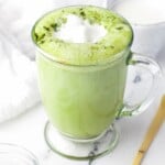 Matcha latte served in a glass mug, and matcha powder in small bowl on the side