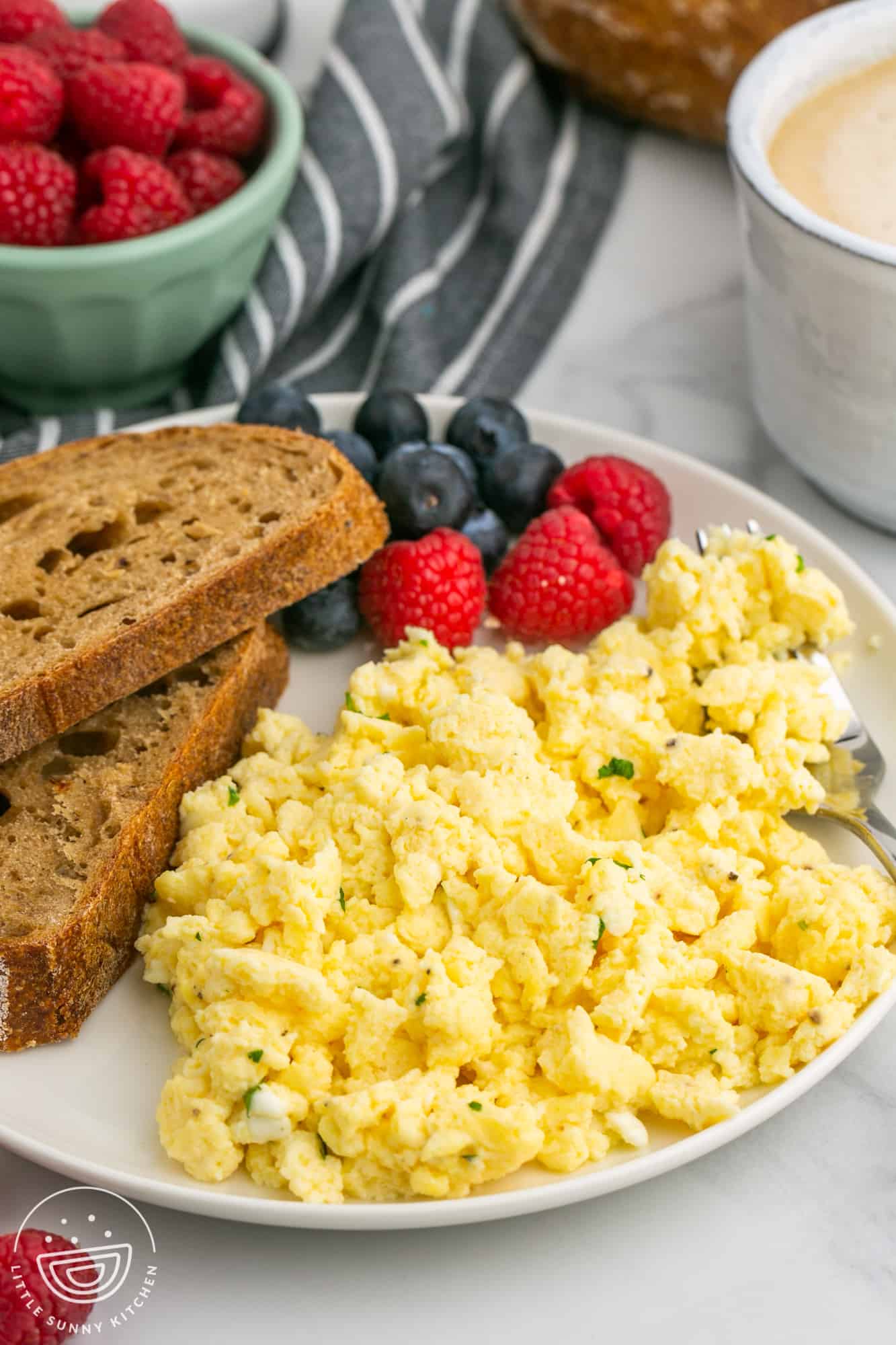 a plate of eggs with cottage cheese with two slices of toast and fresh berries.