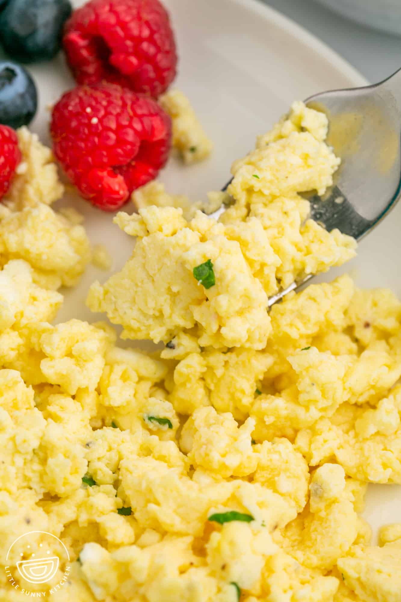 closeup view of cooked scrambled eggs with cottage cheese being eaten with a fork.