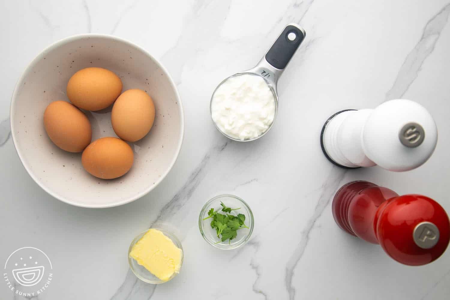 a bowl holding four brown eggs next to a half cup of cottage cheese, salt and pepper shakers, a pat of butter, and fresh parsley.