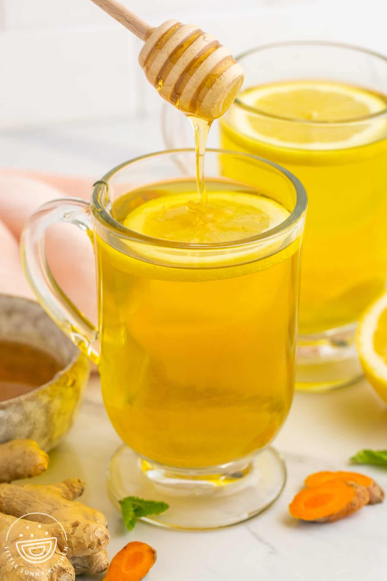 Drizzling honey over turmeric honey tea in a glass cup