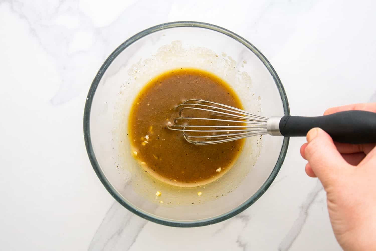 a hand whisking salad dressing in a glass bowl.