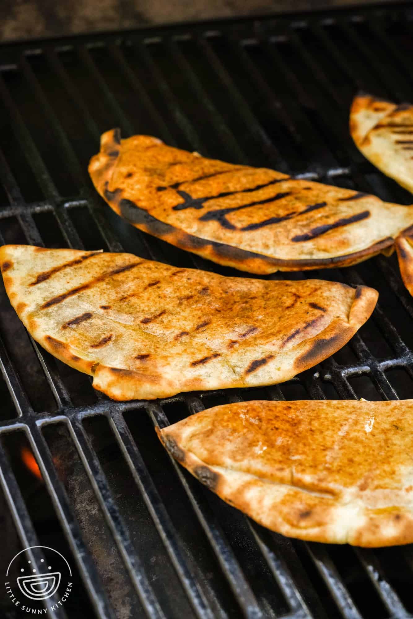Meat stuffed pitas on the grill, with grill marks.