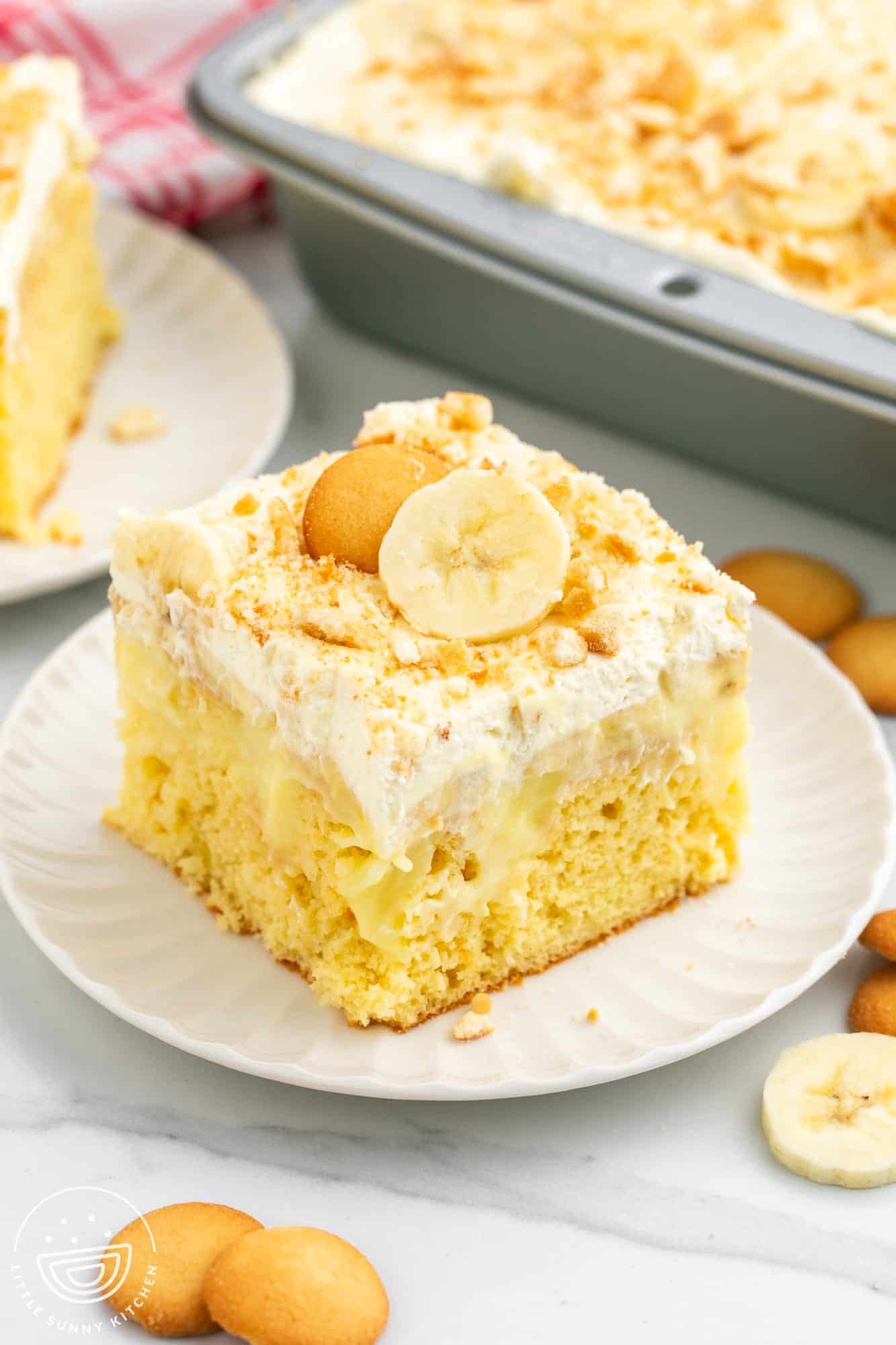 a square piece of banana pudding poke cake, on a plate,cake topped with banana slices and crushed vanilla wafers.