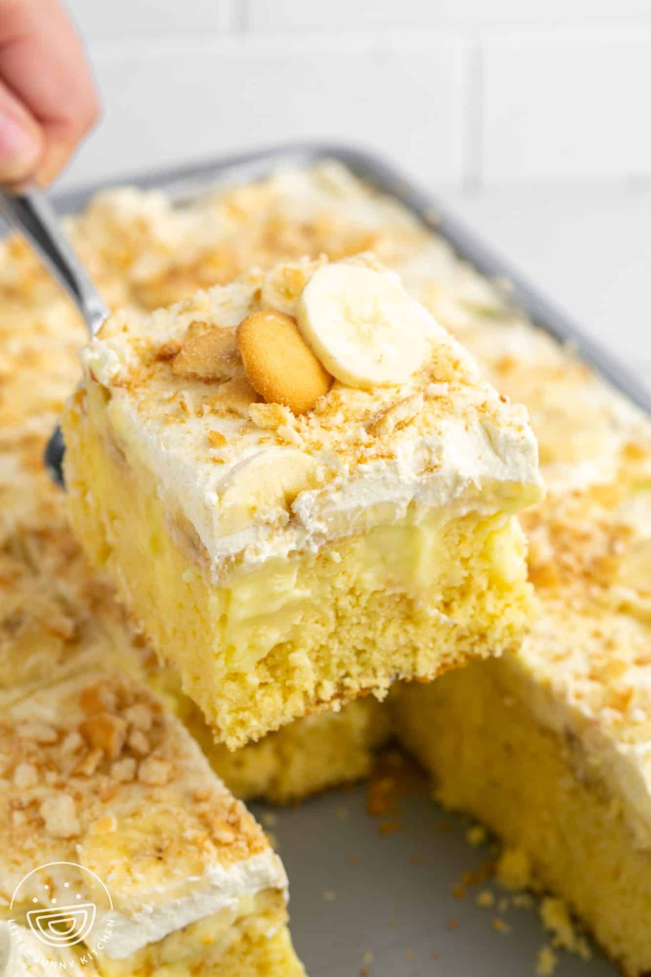 a square of cake topped with whipped cream and bananas being lifted out of the baking pan.