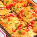 Cheesy enchilada casserole in a pan, cut int squares, garnished with diced tomatoes and cilantro.