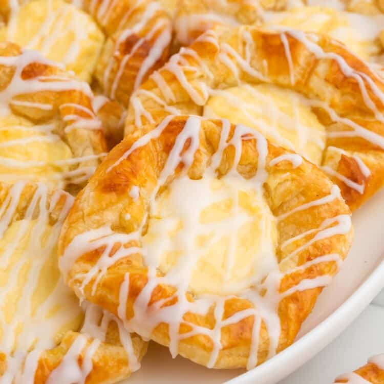 7 cheese danish on an oval platter. They are cheese filled and drizzled with icing.