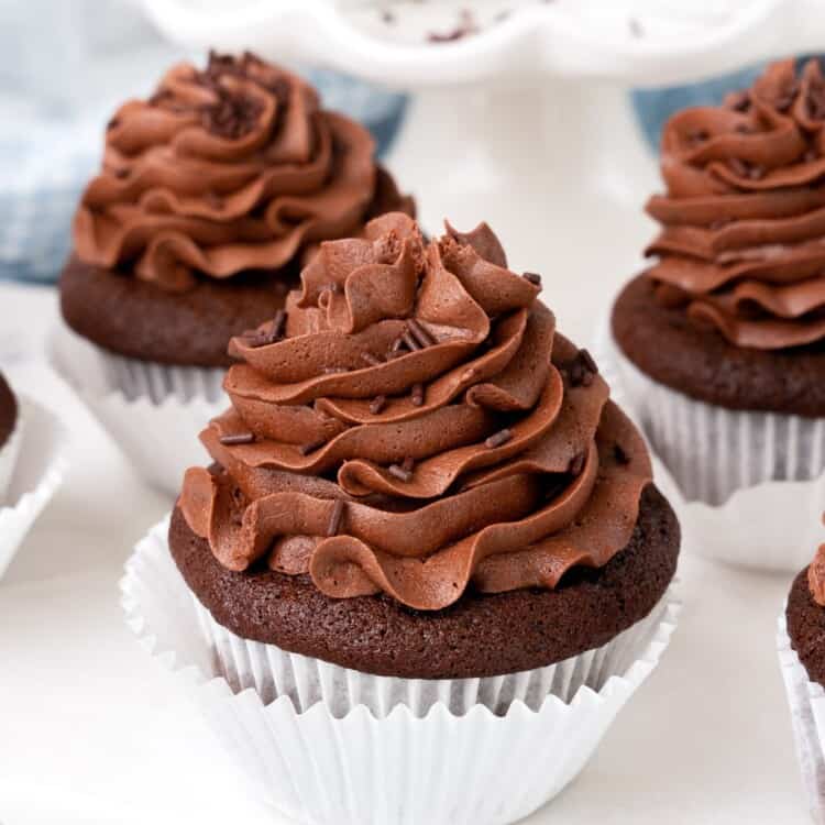 Chocolate cupcakes with chocolate buttercream frosting on a white marble board.