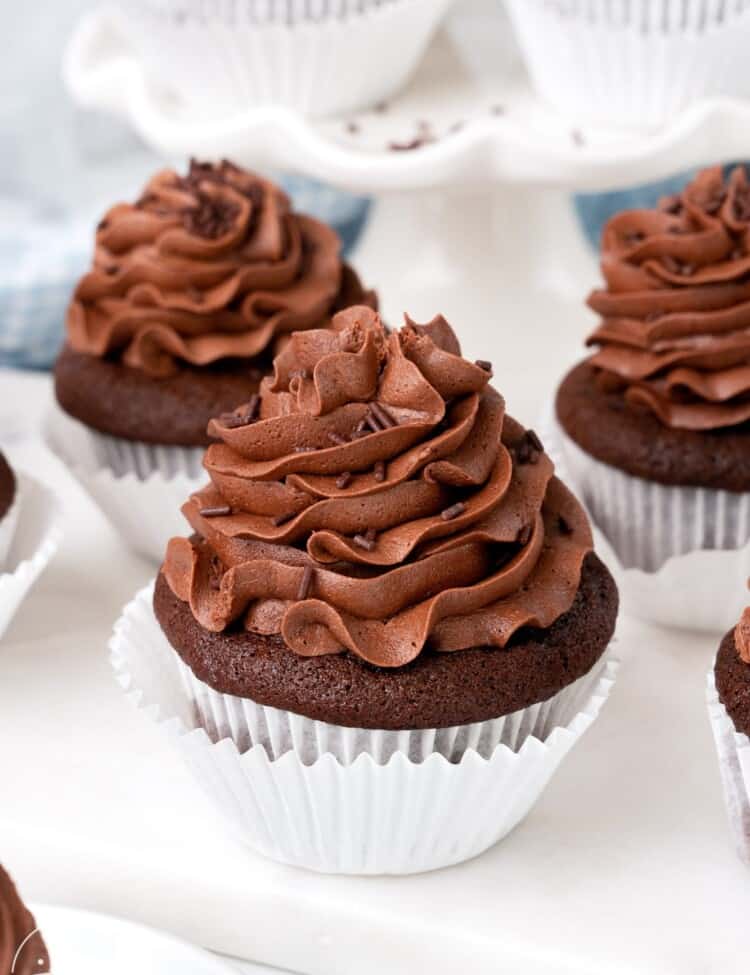 Chocolate cupcakes with chocolate buttercream frosting on a white marble board.