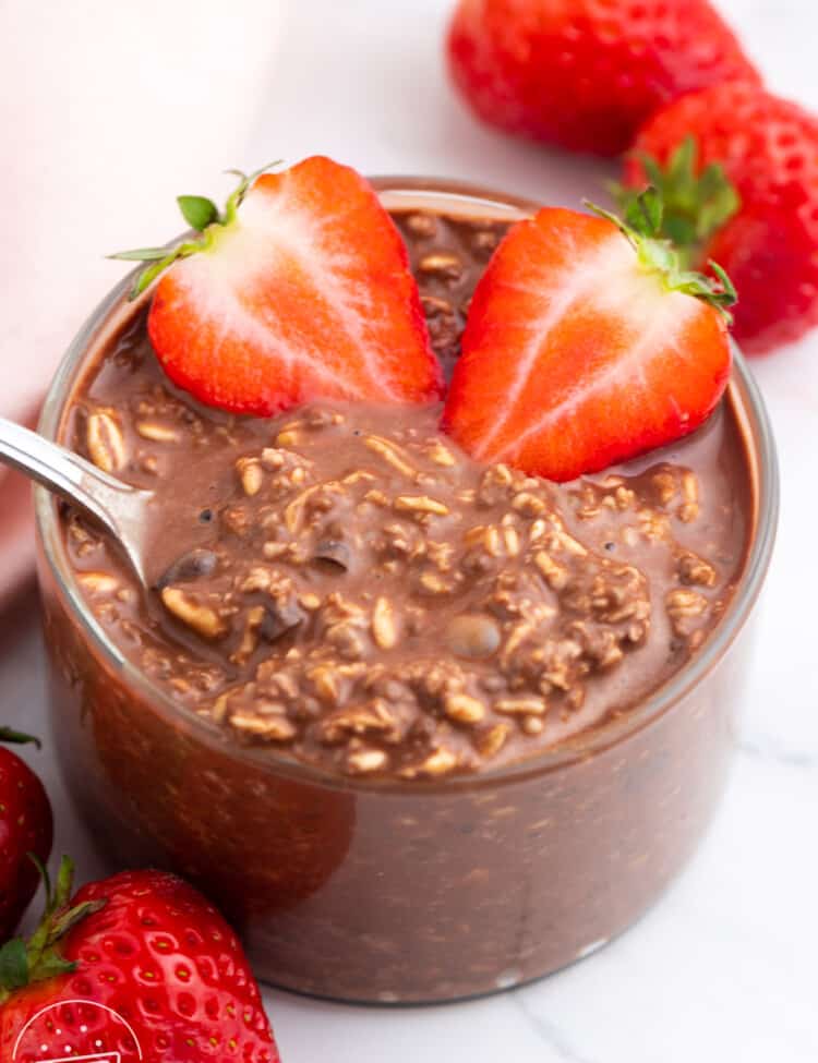 a clear glass bowl of chocolatey overnight oats with sliced strawberries.