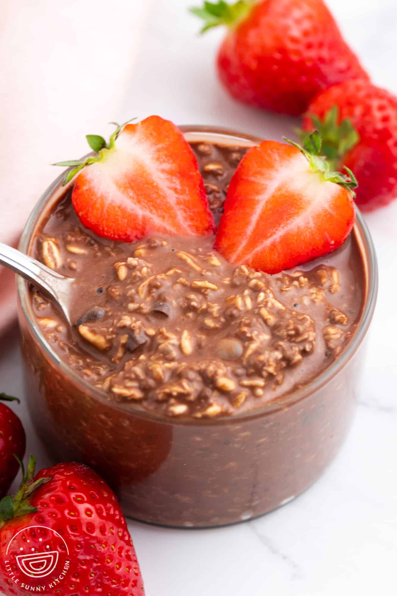a clear glass bowl of chocolatey overnight oats with sliced strawberries. 