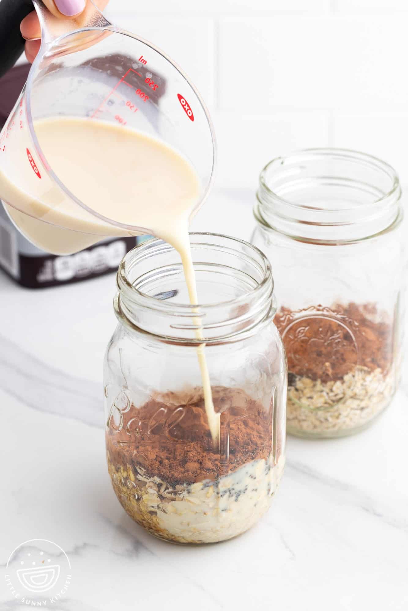 a pitcher pouring milk into mason jars filled with oats and cocoa.