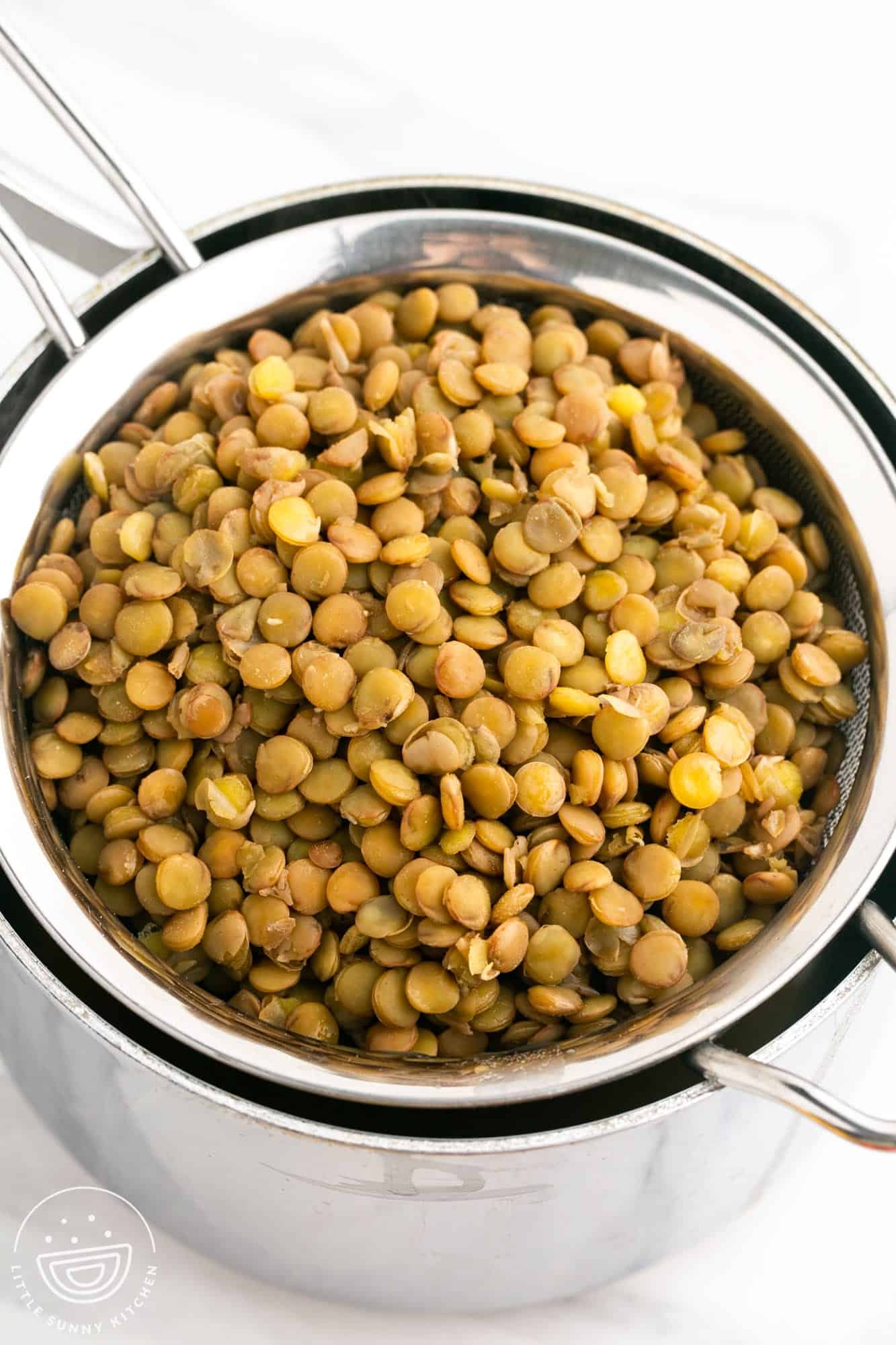 cooked lentils draining in a sieve over a pot.